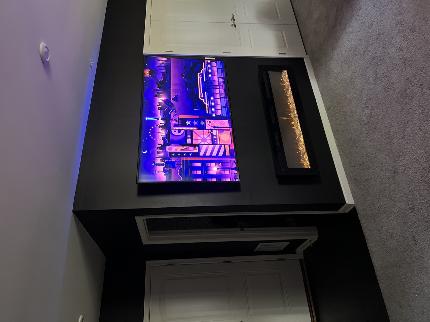 A finished media wall at night, the mounted screen glowing above a fireplace